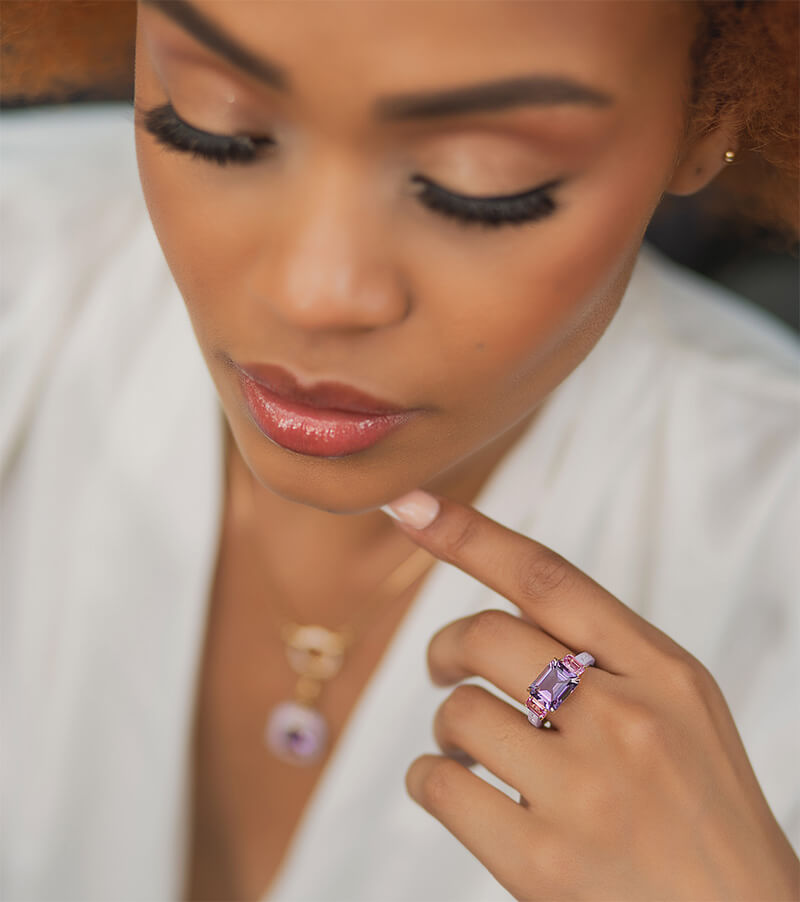 model wearing 3 stone ring with amethyst and sapphires set in 18 carat gold and light purple ceramic